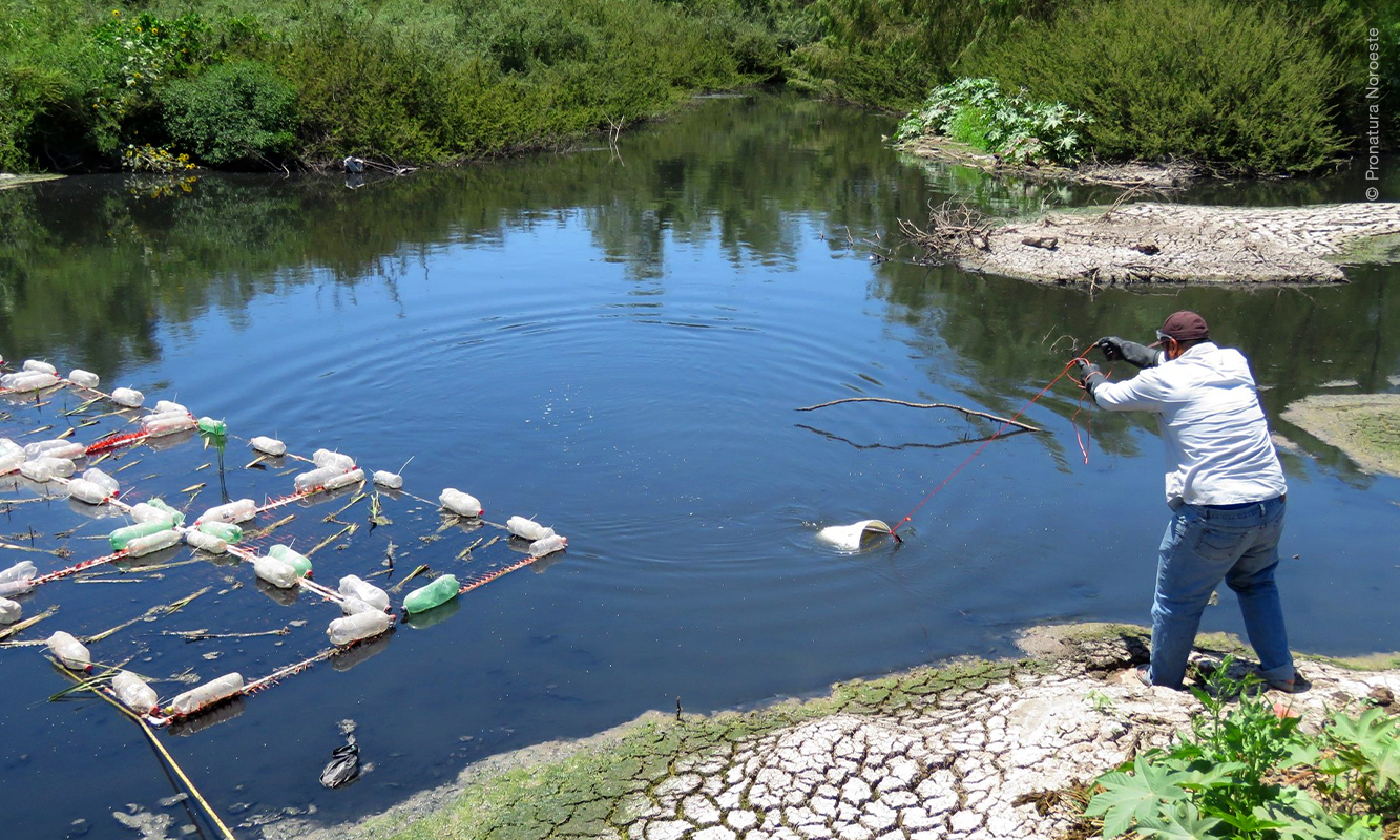 Trabajador lanza una cubeta amarraza a un lazo en la orilla del cauce del agua, para obtener muestra.