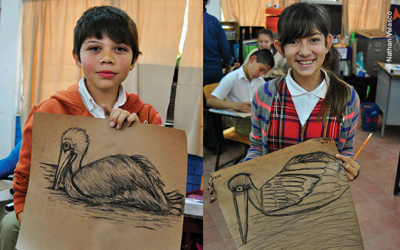 Niño y niña mostrando un dibujo, resultado del taller El ambiente marino y la pesca.
