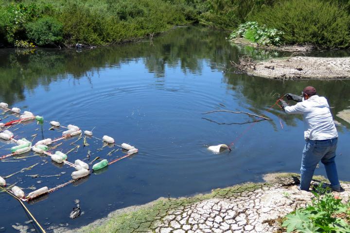 Trabajador lanza una cubeta amarraza a un lazo en la orilla del cauce del agua, para obtener muestra.